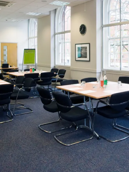 A conference room with multiple tables and black chairs, each table set with water bottles and glasses. A projection screen reads "Woburn House."
