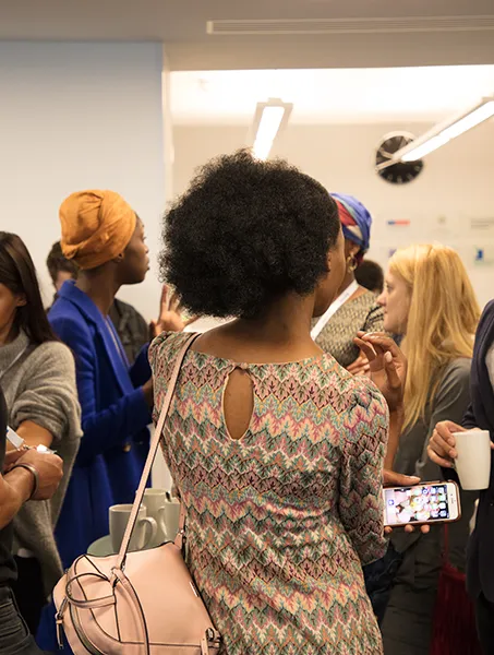 A group of people are engaged in conversation at an indoor networking event, with some holding cups and wearing event badges.