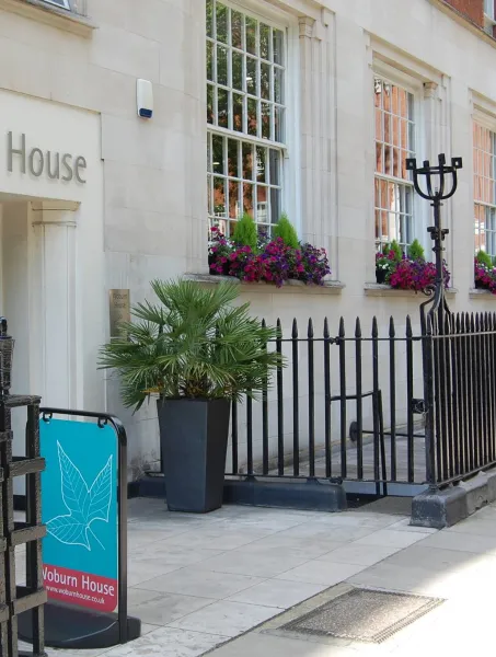 Entrance to Woburn House, featuring cream stone facade, large windows with vibrant pink and purple flowers, and decorative black railings.