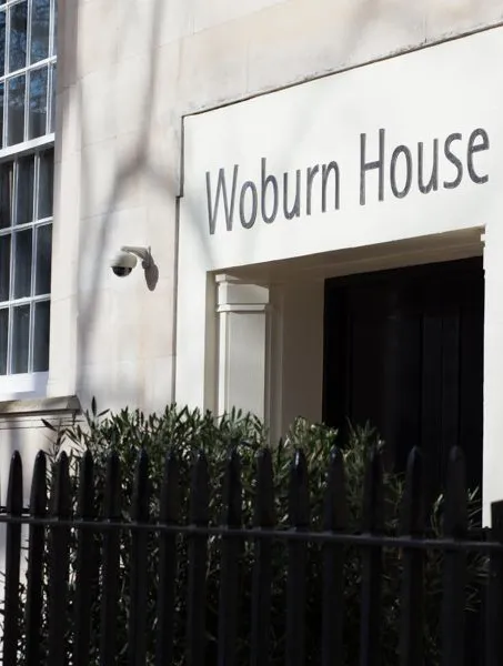 Elegant building entrance labeled "Woburn House." Features large windows, stone facade, and ornate black iron fence, conveying a sense of sophistication.