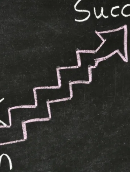 A stick figure climbs chalk-drawn stairs on a blackboard, moving from the word "Plan" at the bottom to "Success" at the top, symbolizing progress.