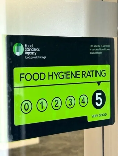Bright green Food Hygiene Rating sticker with a score of 5, marked "Very Good," issued by the Food Standards Agency, displayed on a clear surface.
