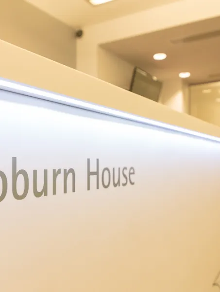 Lobby of Woburn House with a modern, white reception desk prominently displaying the name. A person stands in the blurred background, conveying a formal atmosphere.