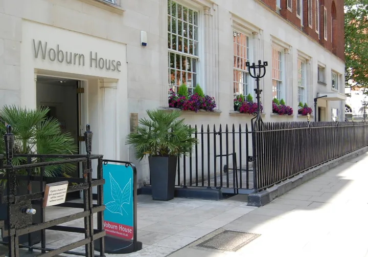 Entrance to Woburn House, featuring cream stone facade, large windows with vibrant pink and purple flowers, and decorative black railings.